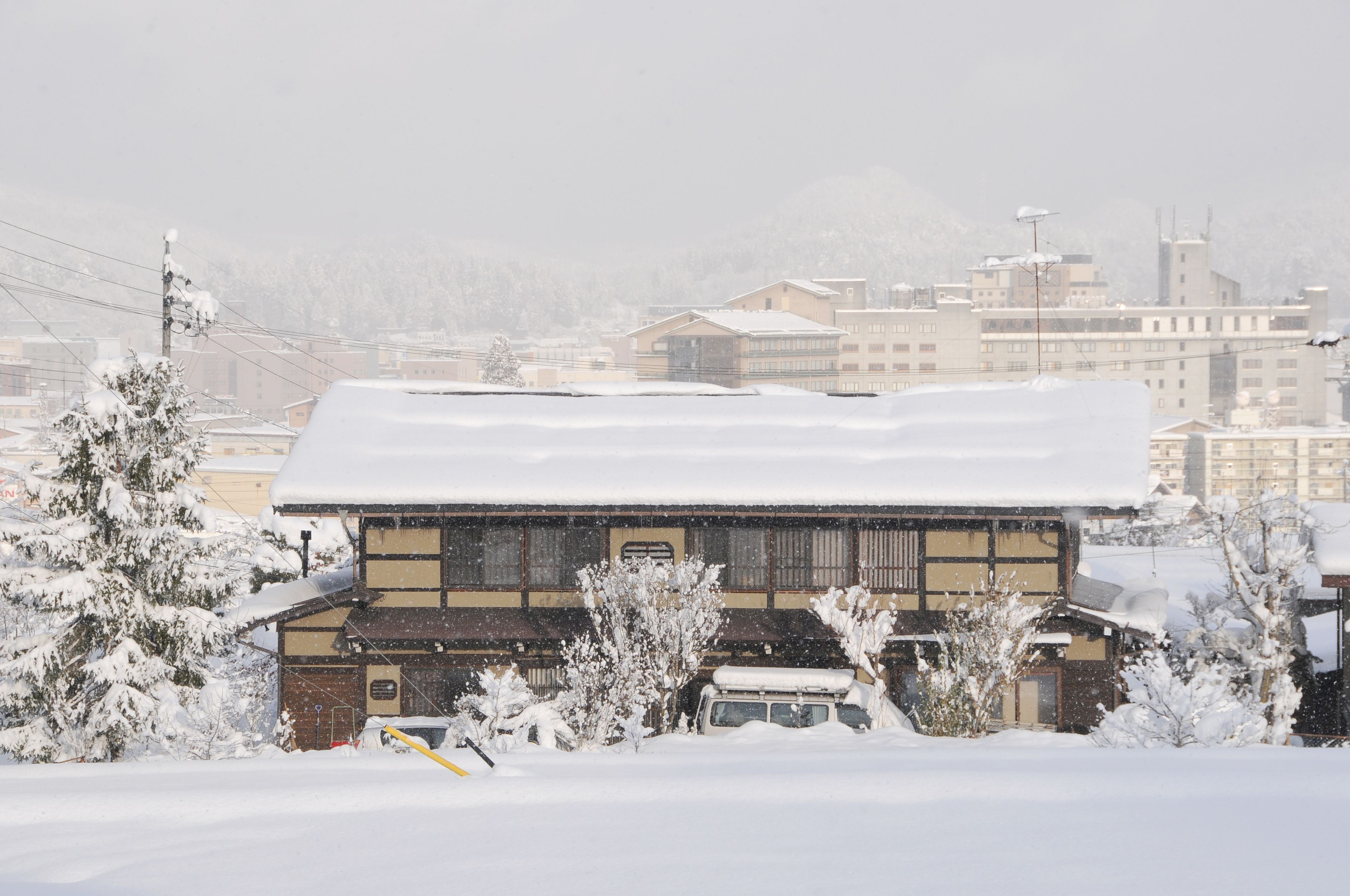 Un edificio tradicional con techo nevado, rodeado de árboles cargados de nieve y un vehículo estacionado.