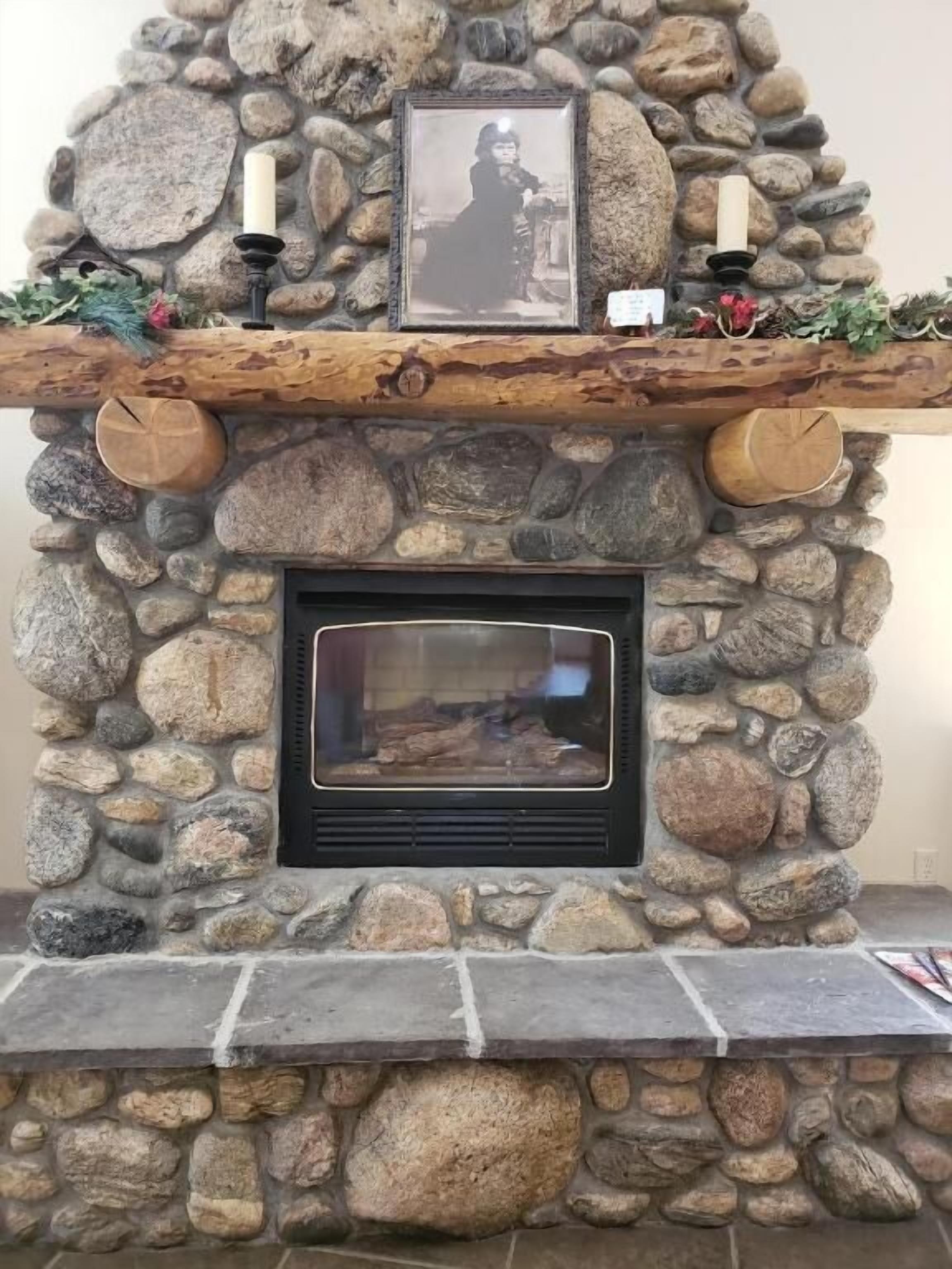 A stone fireplace with a framed picture above, candles, and a log fire.