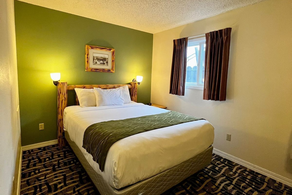 Quarto de hotel com uma cama, paredes verdes, um quadro emoldurado e uma janela com cortinas.