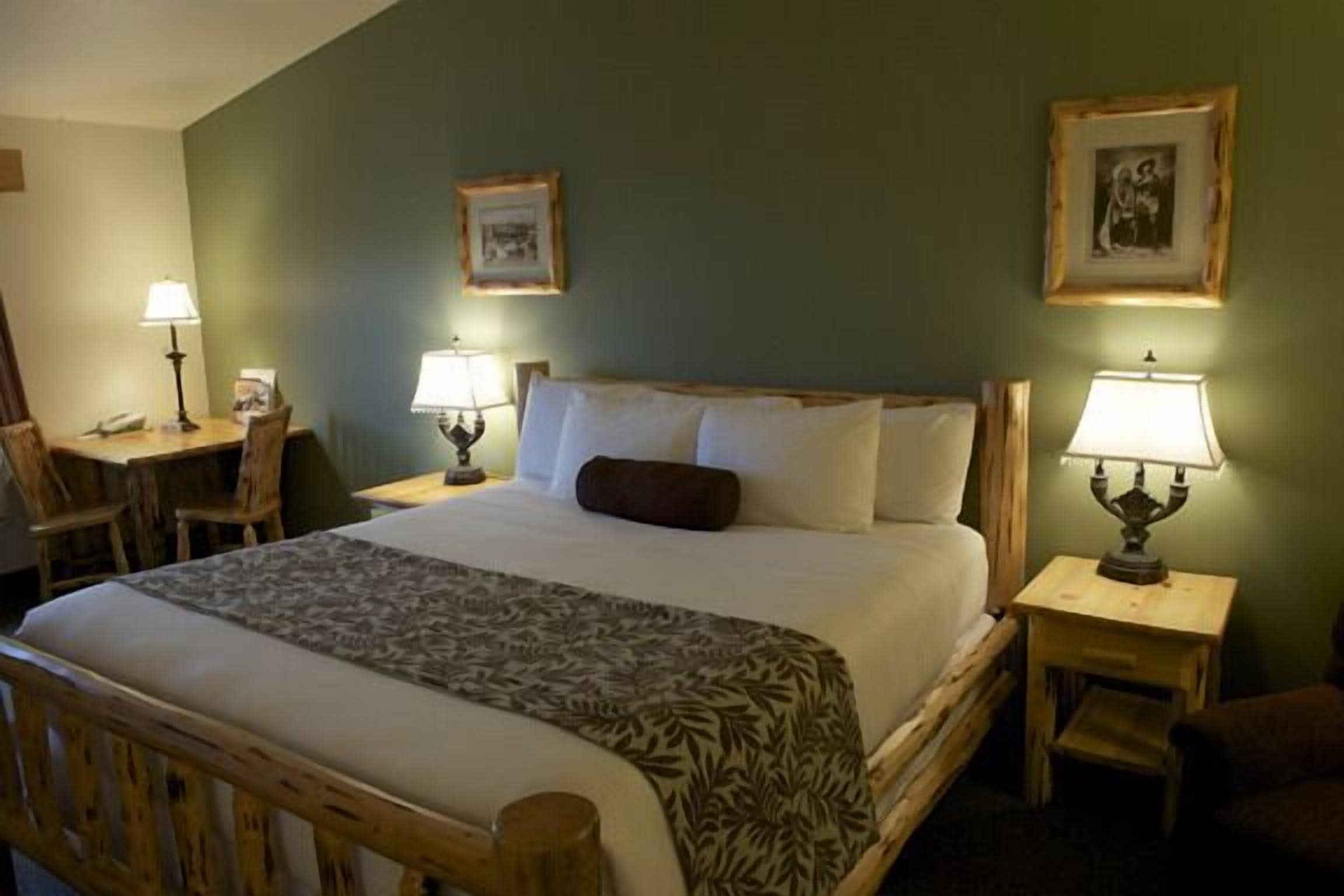 A hotel room with a large bed, two bedside tables with lamps, a chair, and a desk with a telephone.