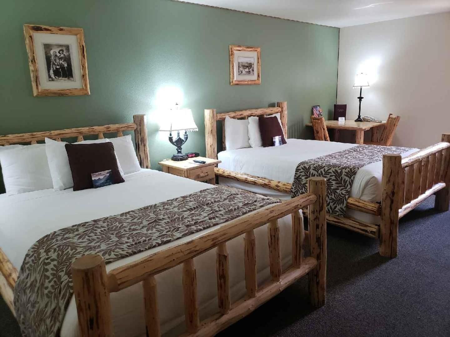 A hotel room with two wooden beds, a nightstand with a lamp, and a small table with a lamp.