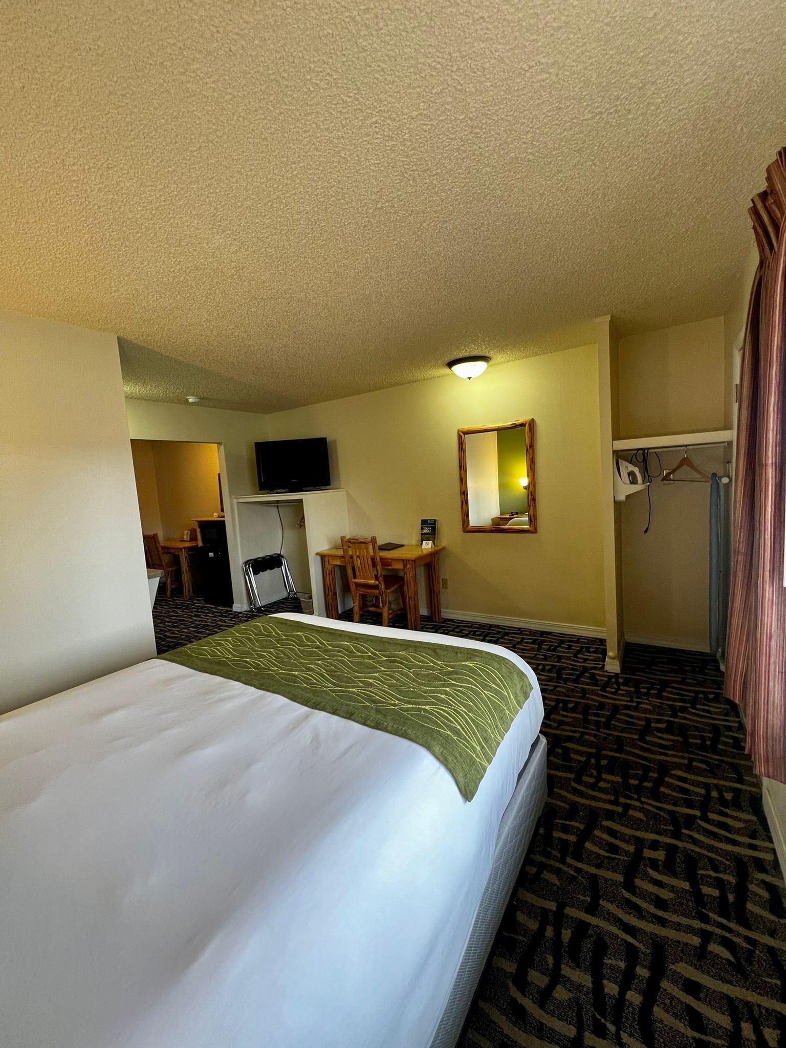Une chambre d’hôtel avec un grand lit, un bureau avec une chaise, une télévision, un miroir et une armoire.