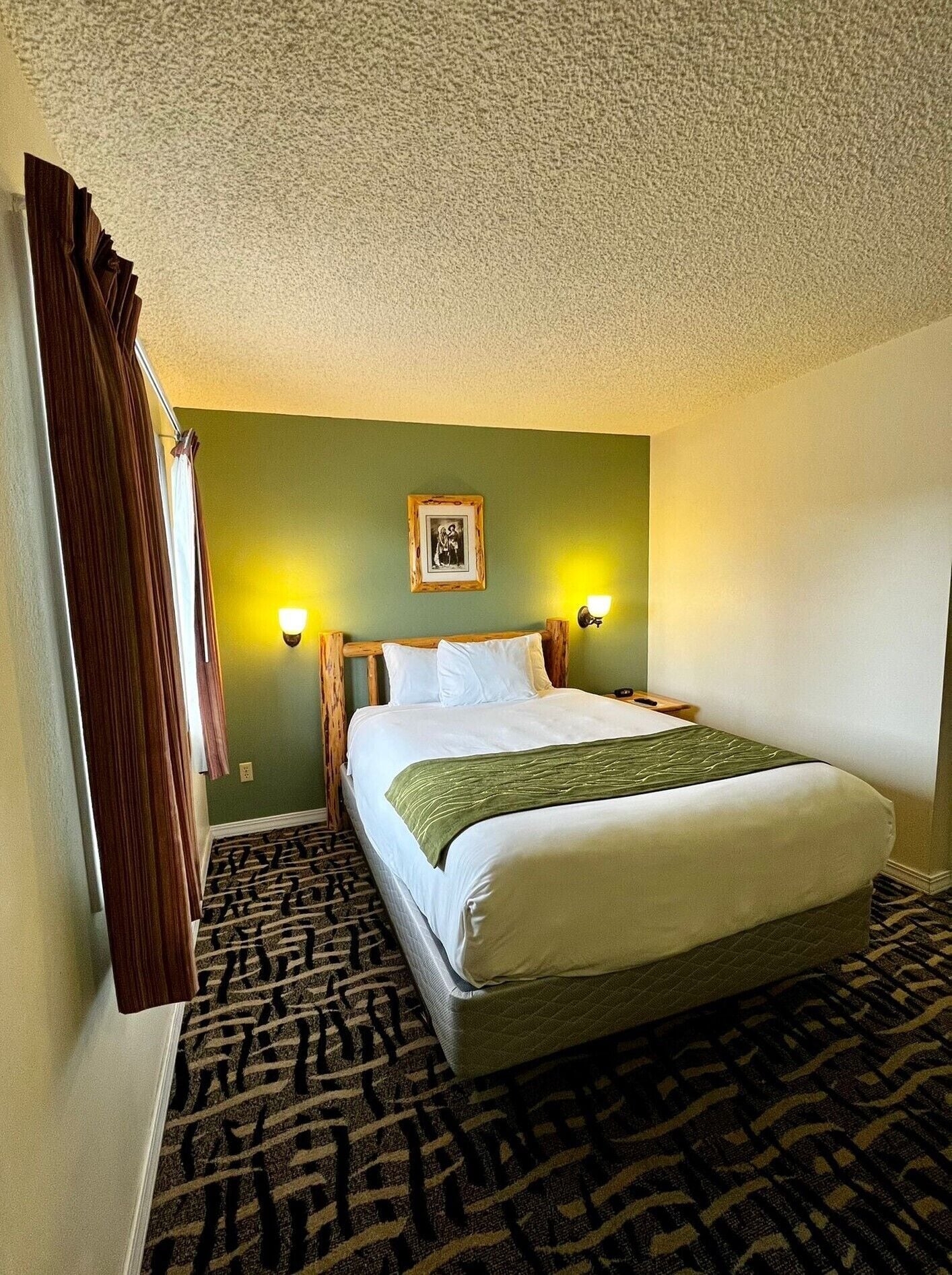 A hotel room with a bed, two bedside lamps, a framed picture on the wall, and a patterned carpet.