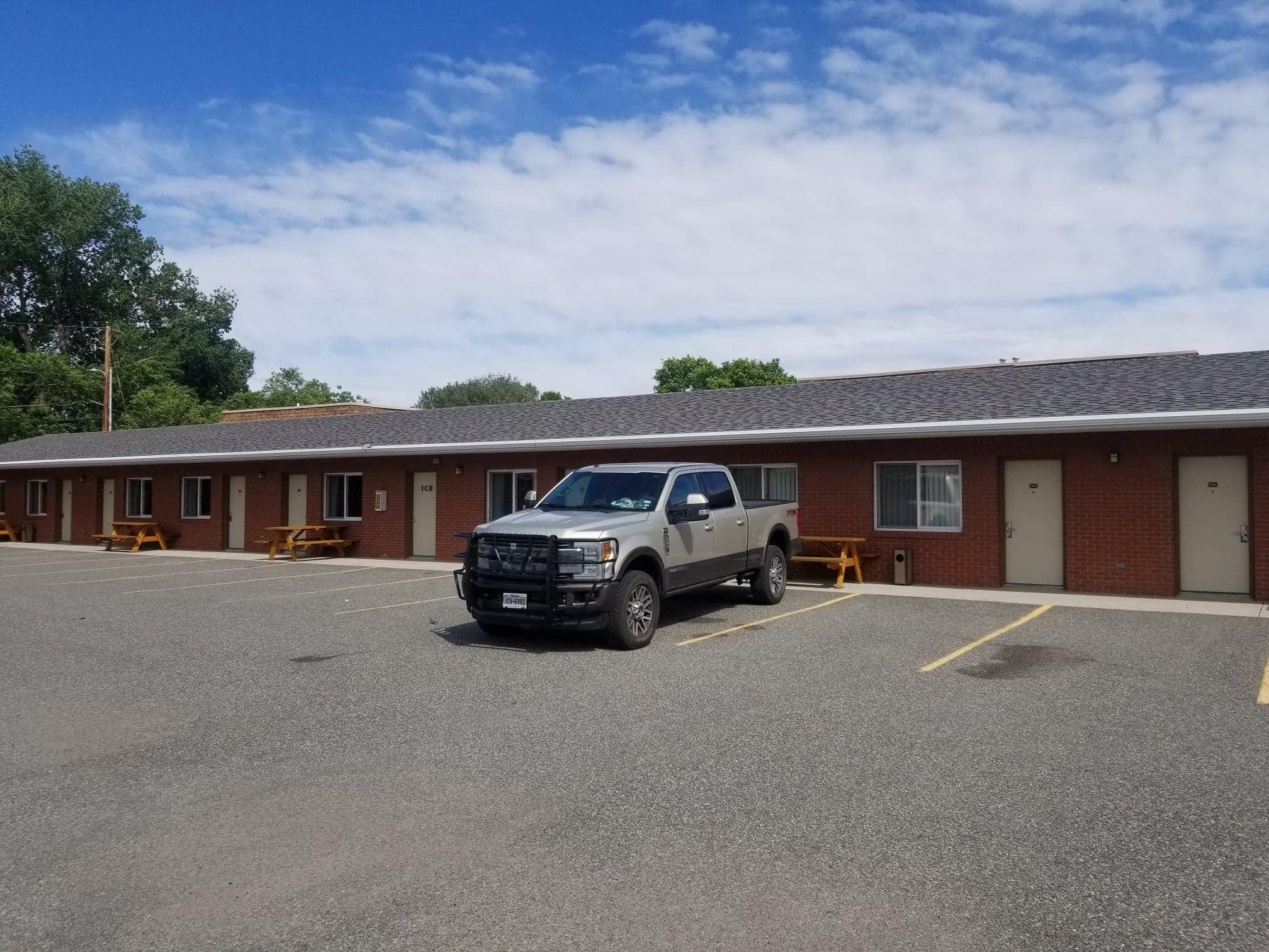 Un motel con estacionamiento, una camioneta pickup y mesas de picnic.