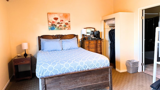 A bedroom with a wooden bed, a nightstand, a dresser, a painting, and a closet.