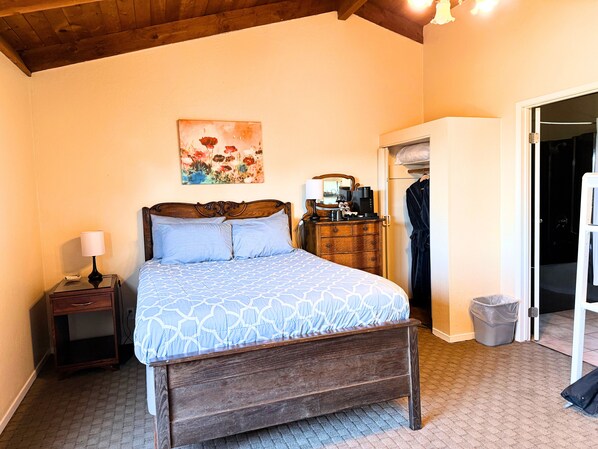 A bedroom with a wooden bed, a nightstand, a dresser, a painting, and a closet.