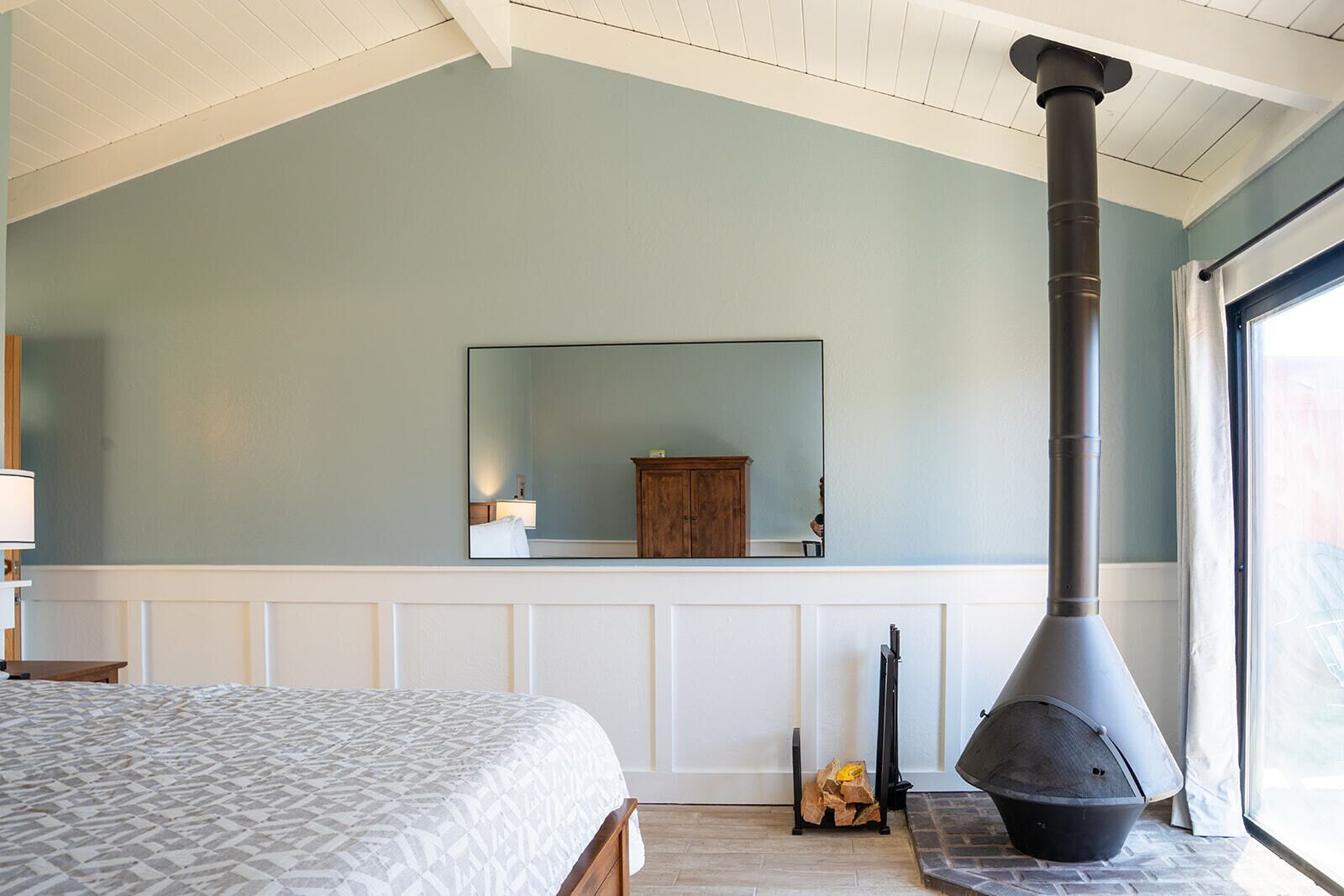 A bedroom with a large bed, a mirror, a fireplace, and a window.