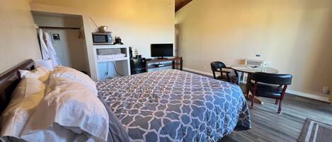 Ein Hotelzimmer mit einem Bett, einem Schreibtisch mit Computer, einem Fernseher und einem Sessel.