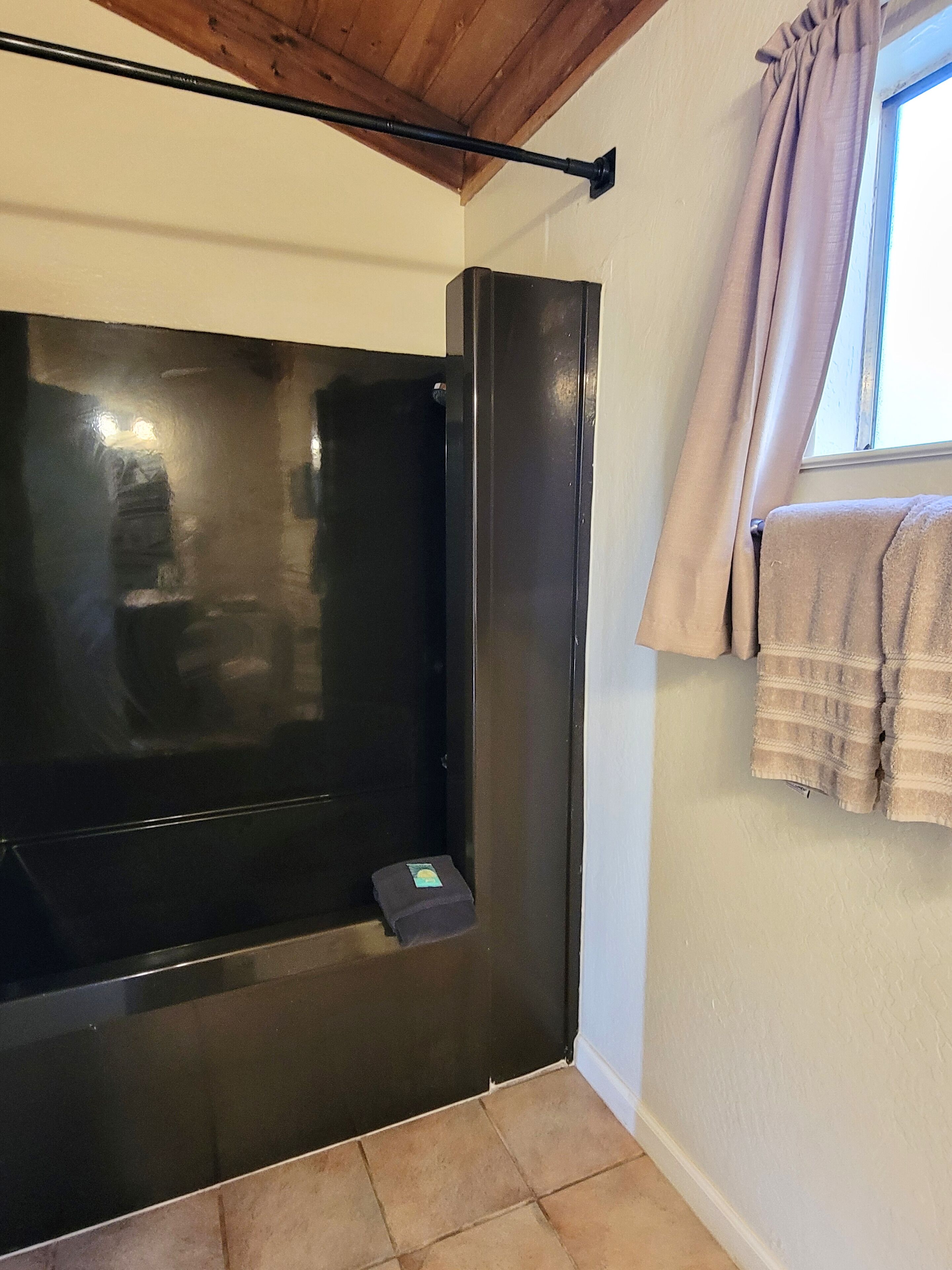 Un bagno con una vasca da bagno nera, un porta asciugamani con un asciugamano e una finestra con tende.