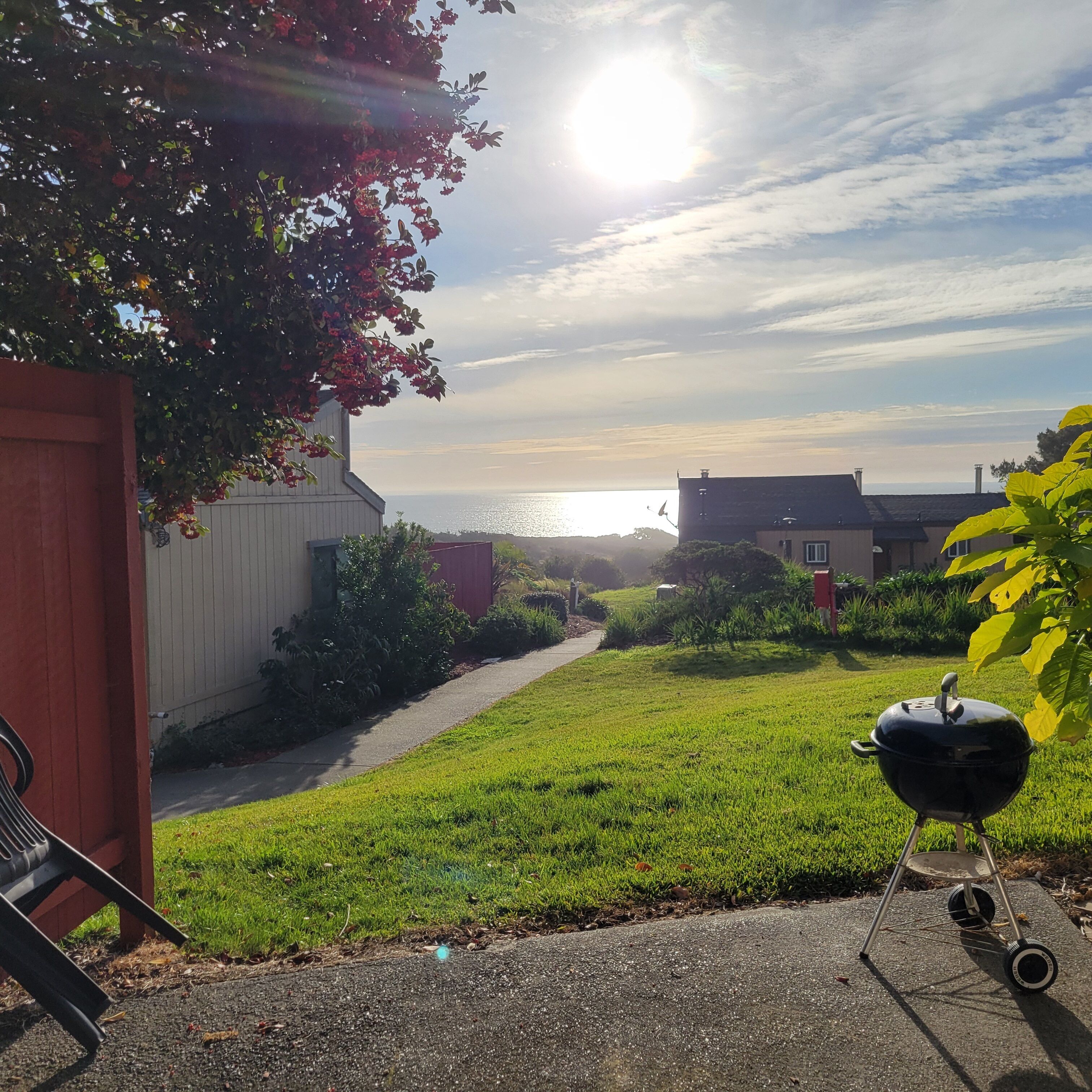 A backyard with a grill, a pathway, and a view of the ocean.