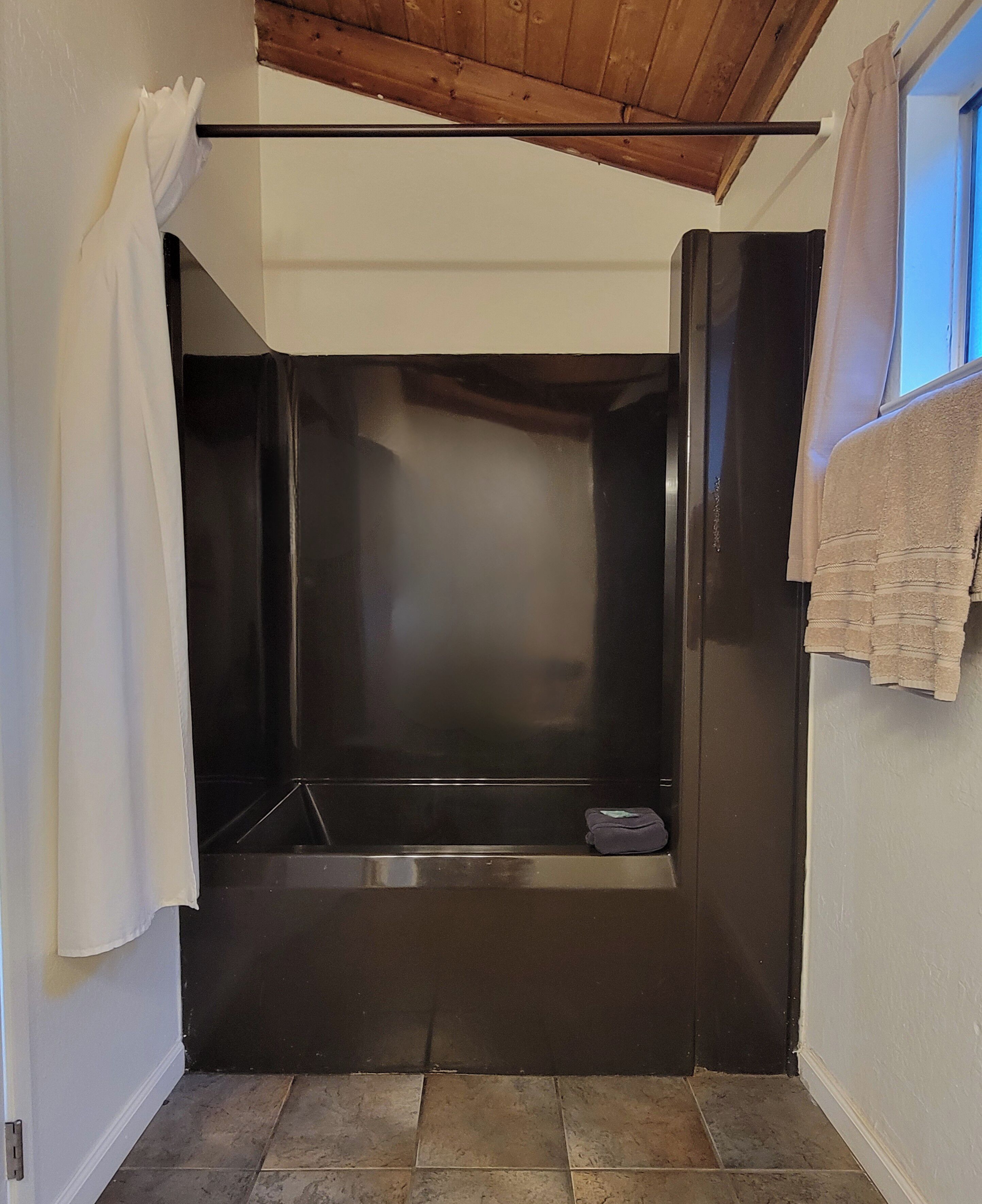A bathroom with a black bathtub, a towel rack, and a window with a curtain.
