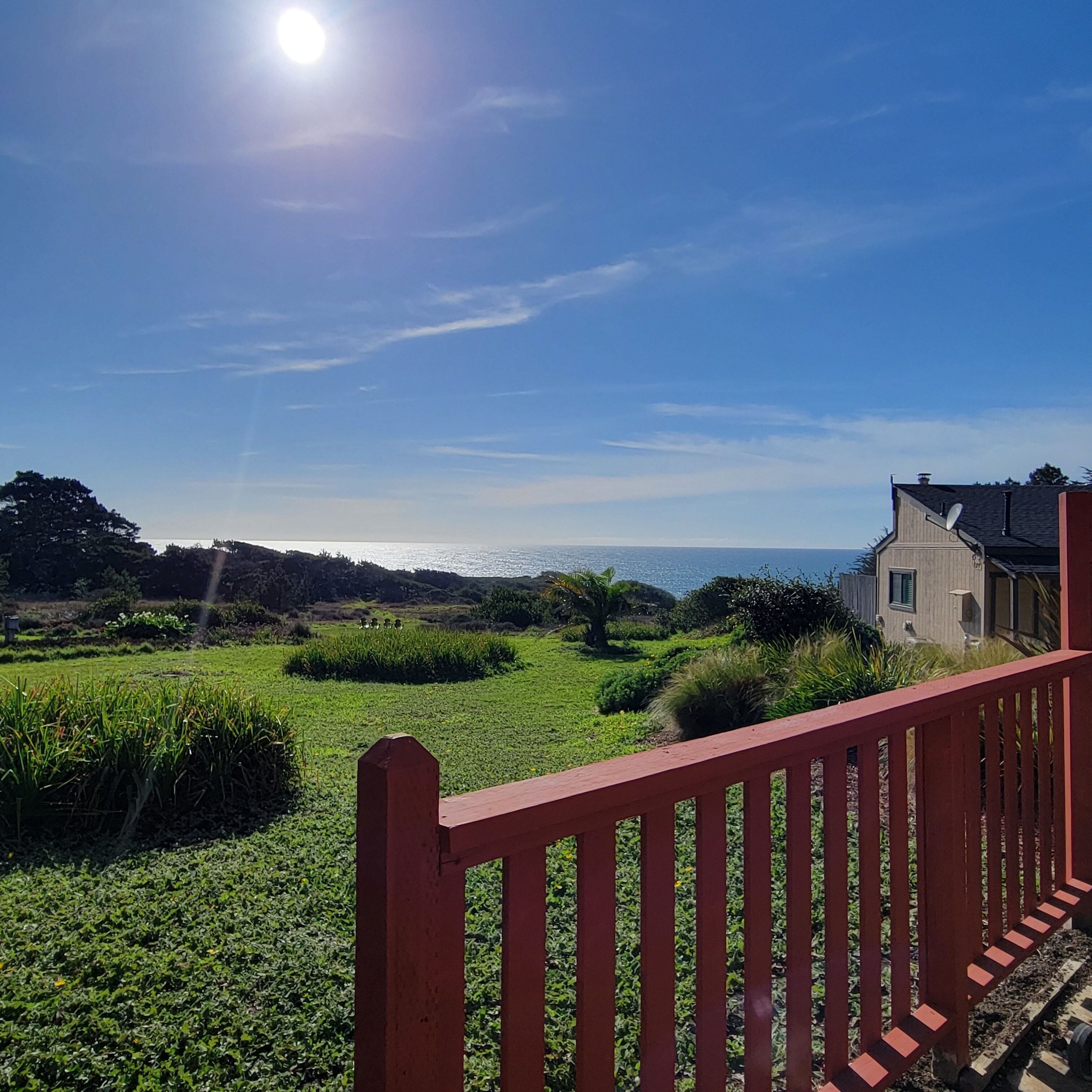 A coastal landscape with a red railing, a white building, and a clear sky.