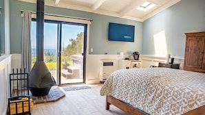 A bedroom with a large bed, a fireplace, a TV, and a view of the outdoors.