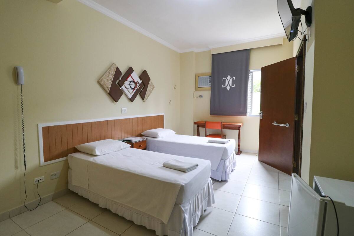 Una habitación de hotel con dos camas, un escritorio, una silla, un televisor y una puerta.