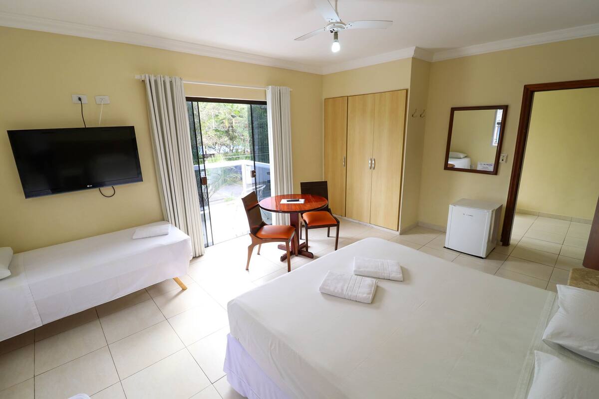 Una habitación de hotel con cama, televisión, una pequeña mesa con sillas, armario y refrigerador.