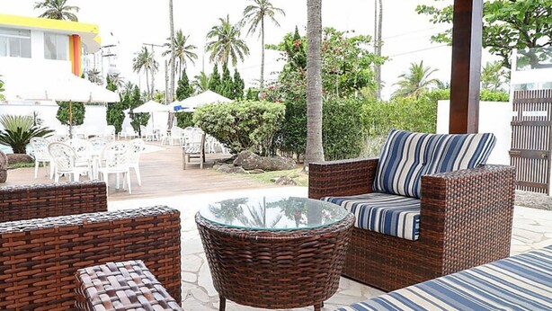 Een terras met rieten meubels, een tafel met glazen blad en witte parasols.