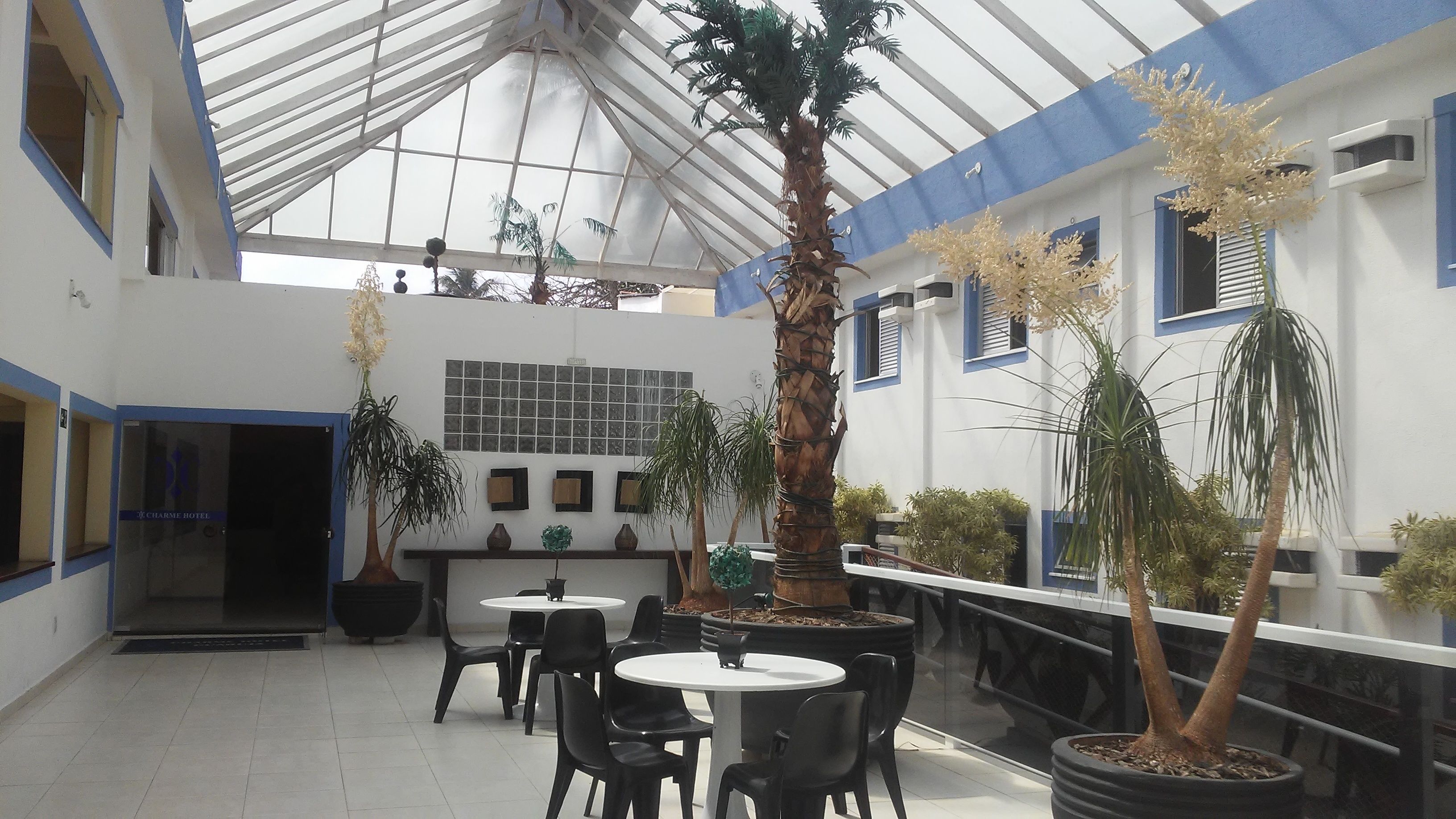 A hotel lobby with a high ceiling, potted plants, and a seating area with tables and chairs.