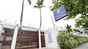 De ingang van Charme Hotel Guarujá met een hek, palmbomen en een naambord.