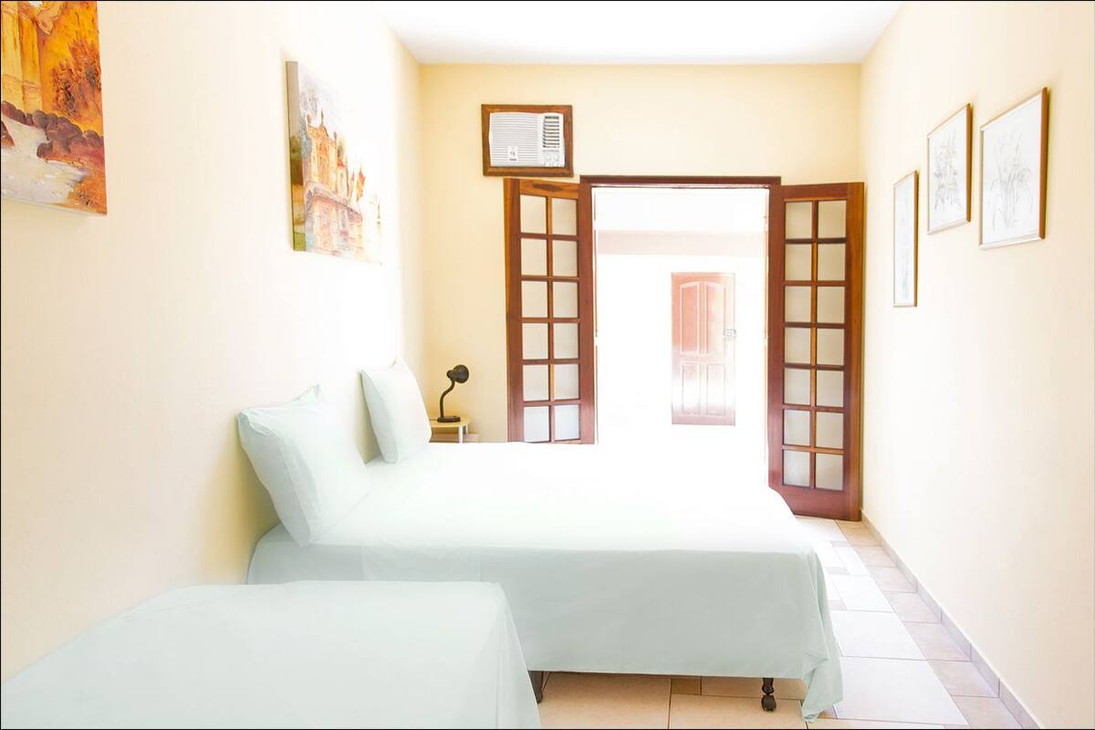 A bedroom with two beds, a nightstand, a lamp, and artwork on the walls.