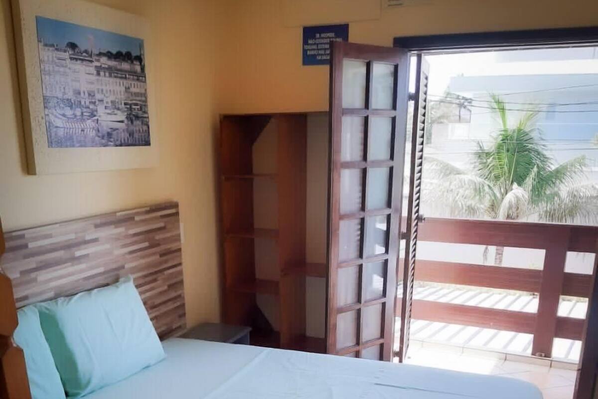 A room with a bed, a wooden headboard, a painting on the wall, and a view of palm trees through an open door.