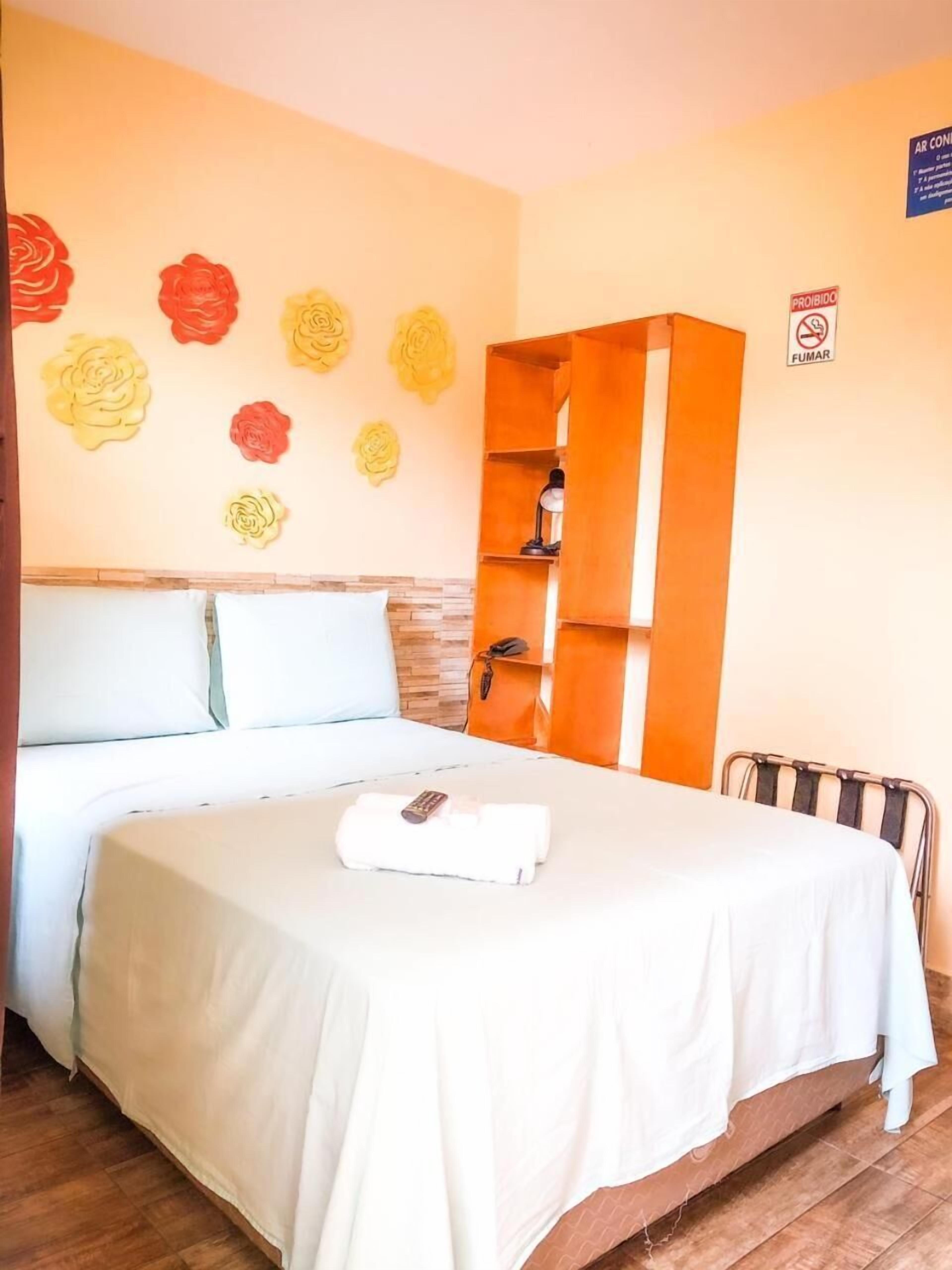 Ein Hotelzimmer mit Bett, Nachttisch, Holzschrank und Wand mit Blumendekoration.