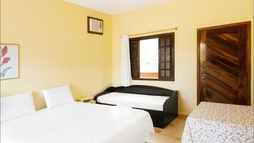 A room with two beds, a window with curtains, a wooden door, and a framed picture on the wall.