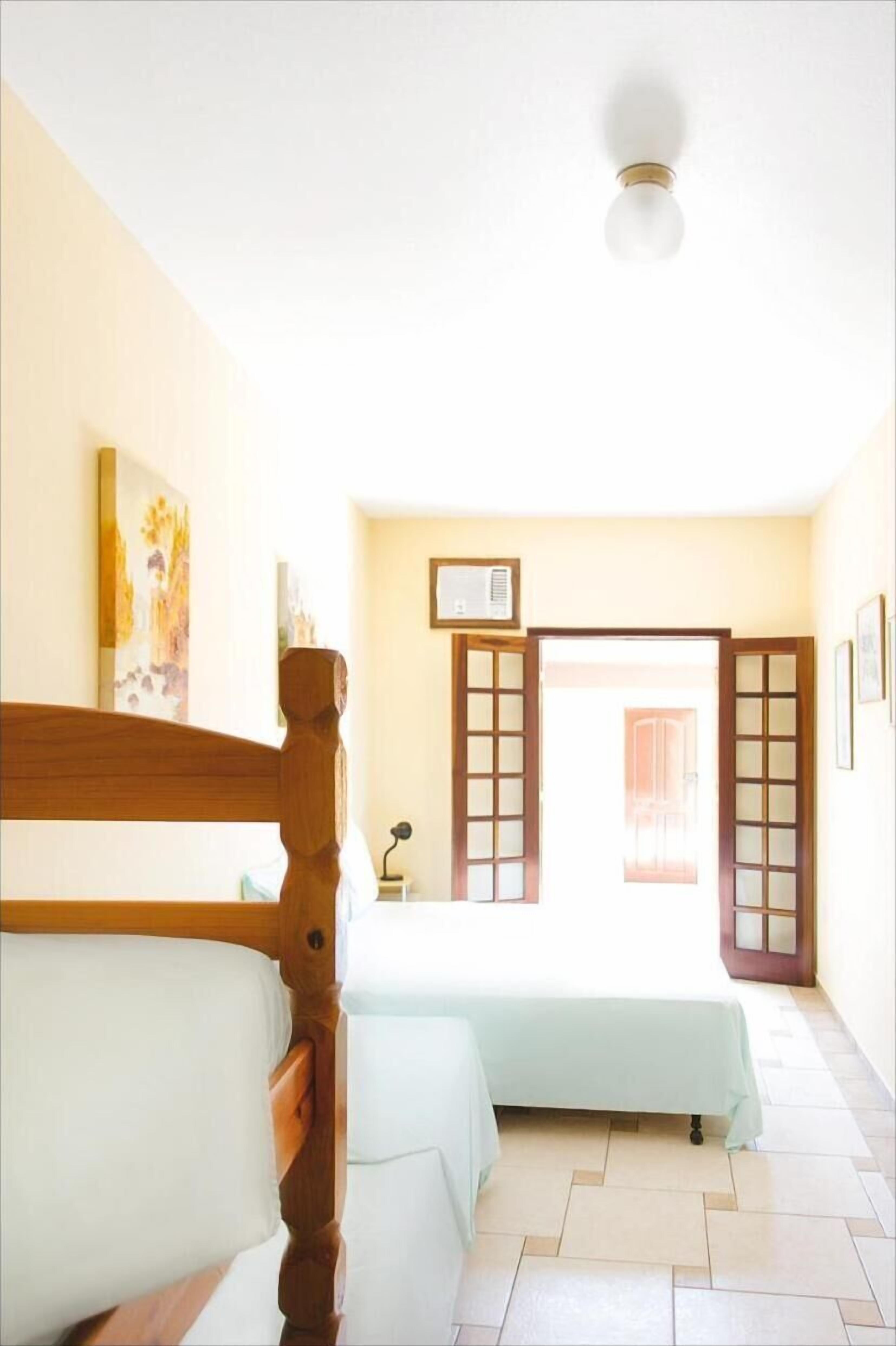 A room with two beds, a wooden headboard, a ceiling light, a framed picture, and a door with glass panels.