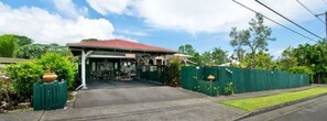 A covered outdoor area with a red roof, surrounded by greenery and a green fence. - Hale Kawehi B&B Guesthouse (Hilo)