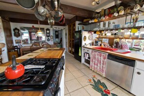 A kitchen with a stove, refrigerator, and various kitchen utensils hanging above. - Hale Kawehi B&B Guesthouse (Hilo)