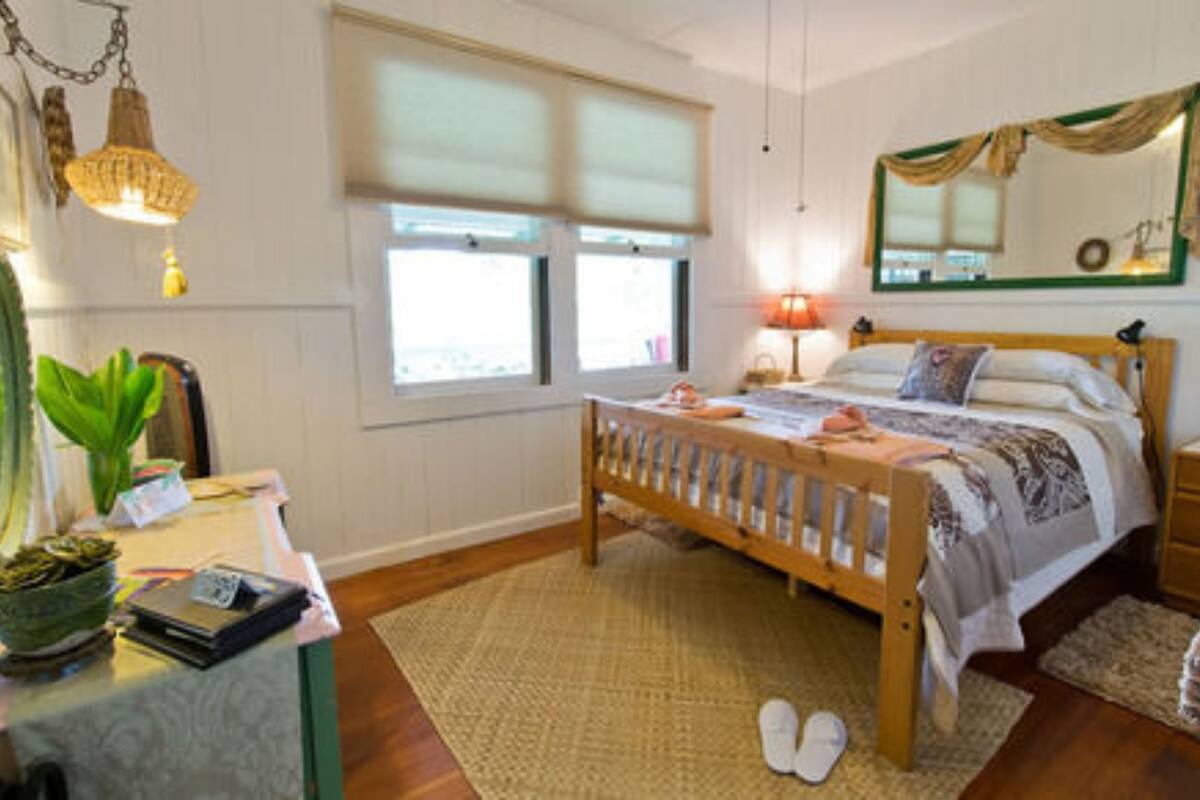 A bedroom with a wooden bed, bedside tables, a desk with a chair, a mirror, and a window with blinds.