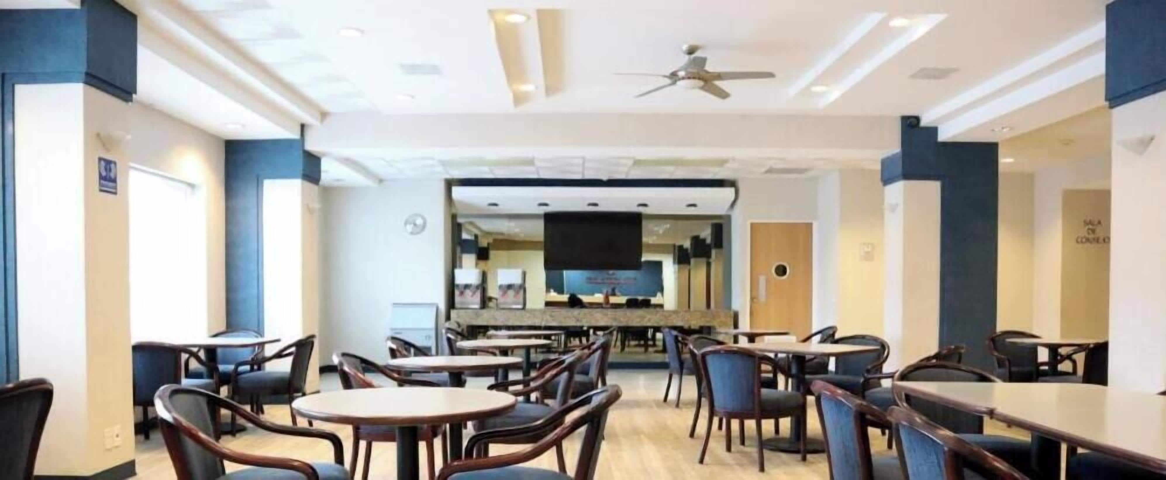 A dining area with tables and chairs, a ceiling fan, and a television screen.