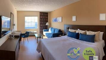 Una habitación de hotel con cama, escritorio, silla, sofá, estantería y televisor.