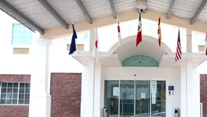 Fachada de edificio con varias banderas, una puerta de cristal y un reloj sobre la puerta.