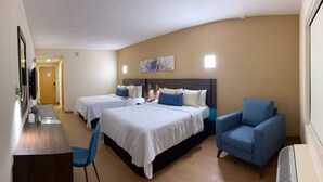 Habitación de hotel con dos camas, un escritorio, una silla y un sillón azul.