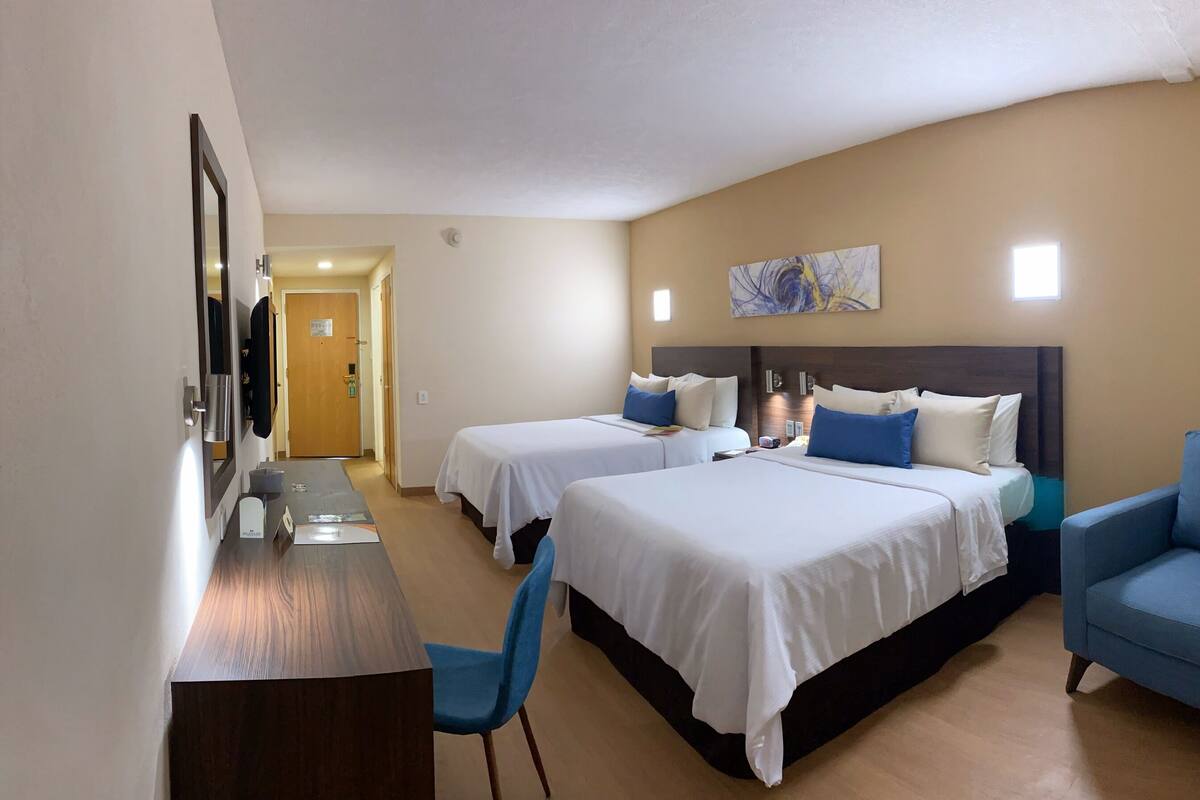 Habitación de hotel con dos camas, un escritorio, una silla y un sillón azul.
