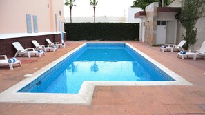 A rectangular swimming pool with a tiled edge, surrounded by white lounge chairs with blue cushions.