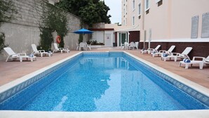 Una piscina con sillas de descanso y una sombrilla azul.