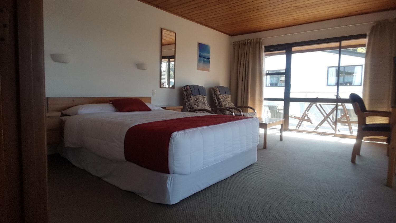 A bedroom with a large bed, two chairs, a small table, and a balcony with a view.