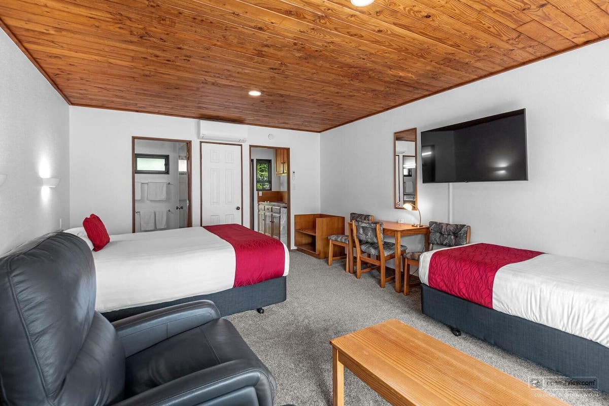 A hotel room with two beds, a sofa, a desk, and a TV.