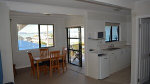 Eine kompakte Küche mit weißen Schränken, einer Mikrowelle und einem Spülbecken. Ein Essbereich mit Tisch und Stühlen ist vorhanden, sowie eine Glastür zu einem Balkon mit Blick auf Gebäude.
