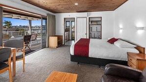 Ein Hotelzimmer mit einem großen Bett, Holzboden, einem Balkon mit Sitzgelegenheit und Blick auf die Stadt.