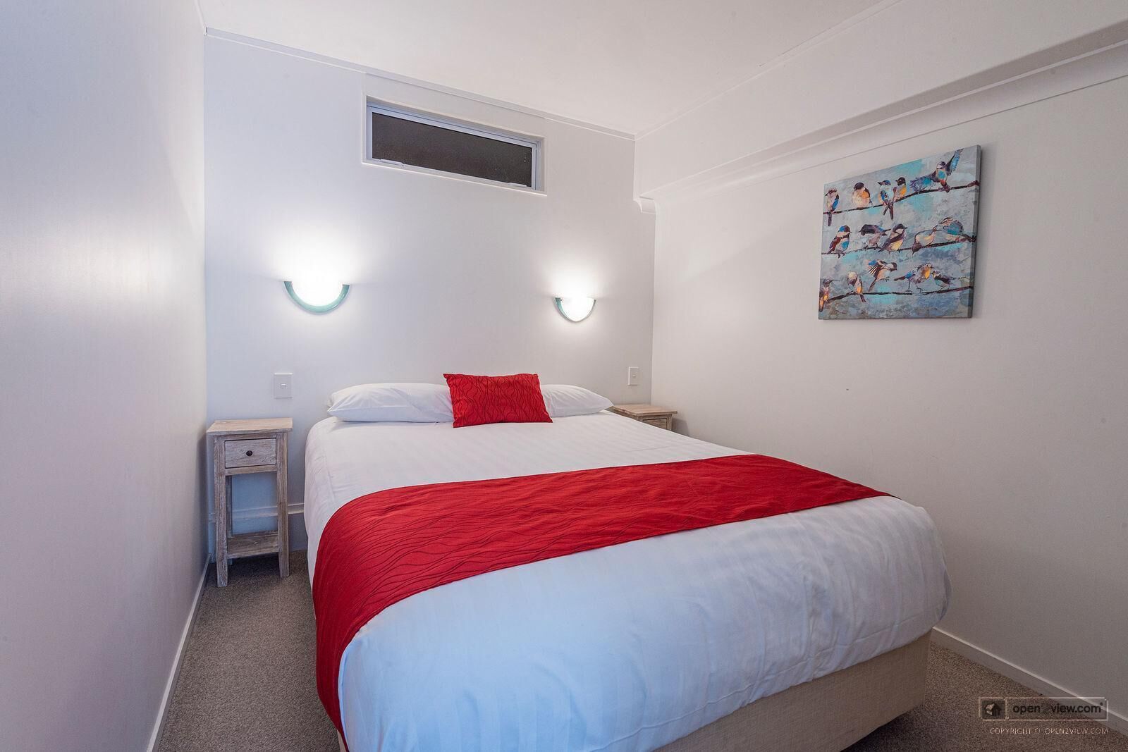 A bedroom with a bed, two bedside tables, a window, and a wall-mounted painting.