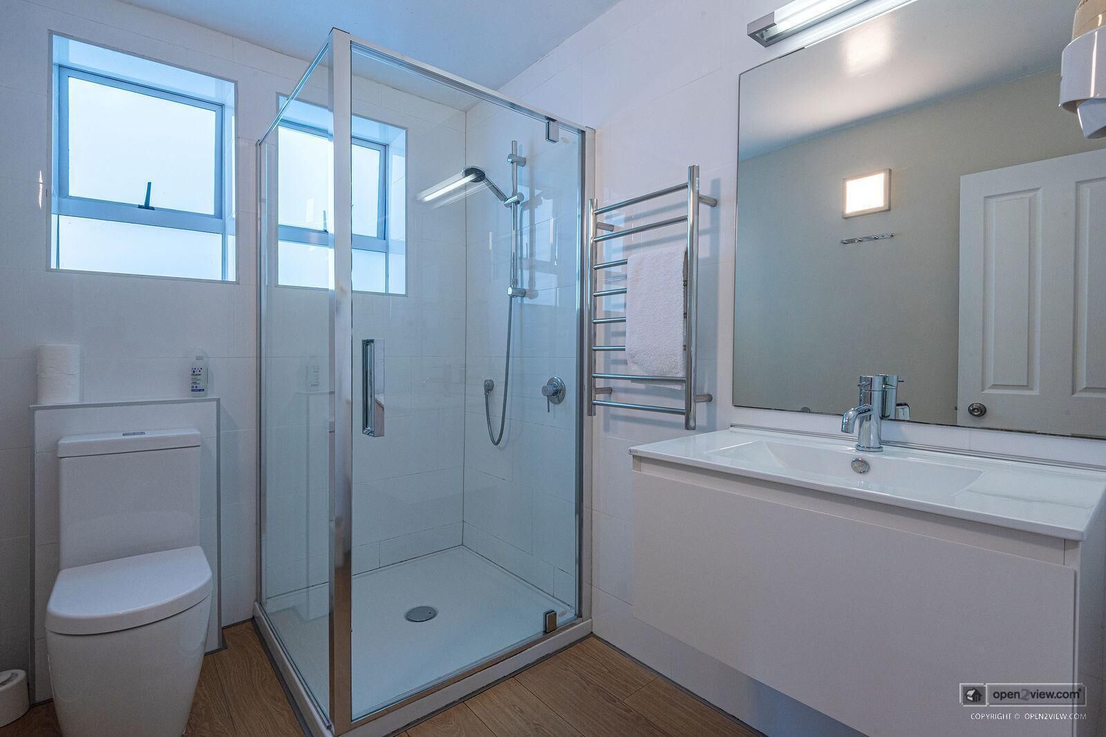 A modern bathroom with a glass shower enclosure, a toilet, a sink with a mirror, and a towel rack.