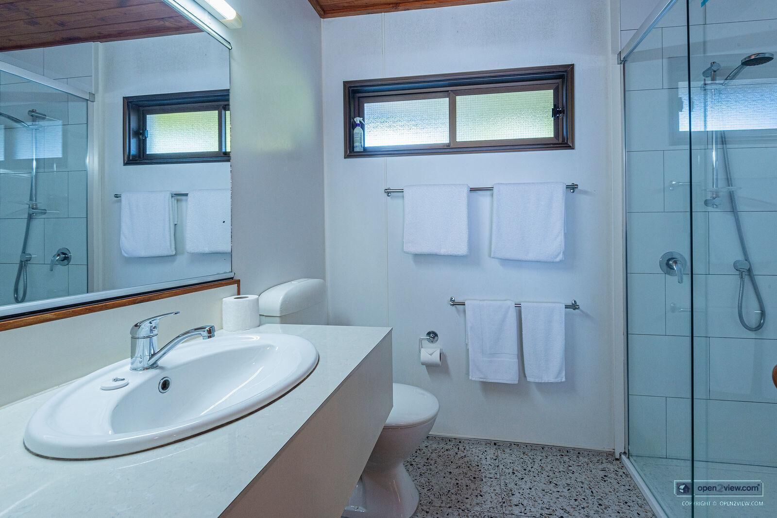 Et moderne badeværelse med en stor vask, toilet og bruser. Der er håndklæder hængende på væggen, og et vindue over toilettet.