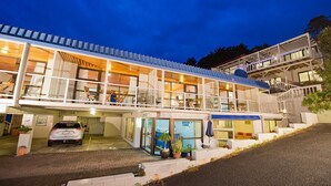 Ein mehrstöckiges Hotel mit überdachter Außenbestuhlung, einem Auto auf der Einfahrt und einer Treppe, die zu den oberen Etagen führt.