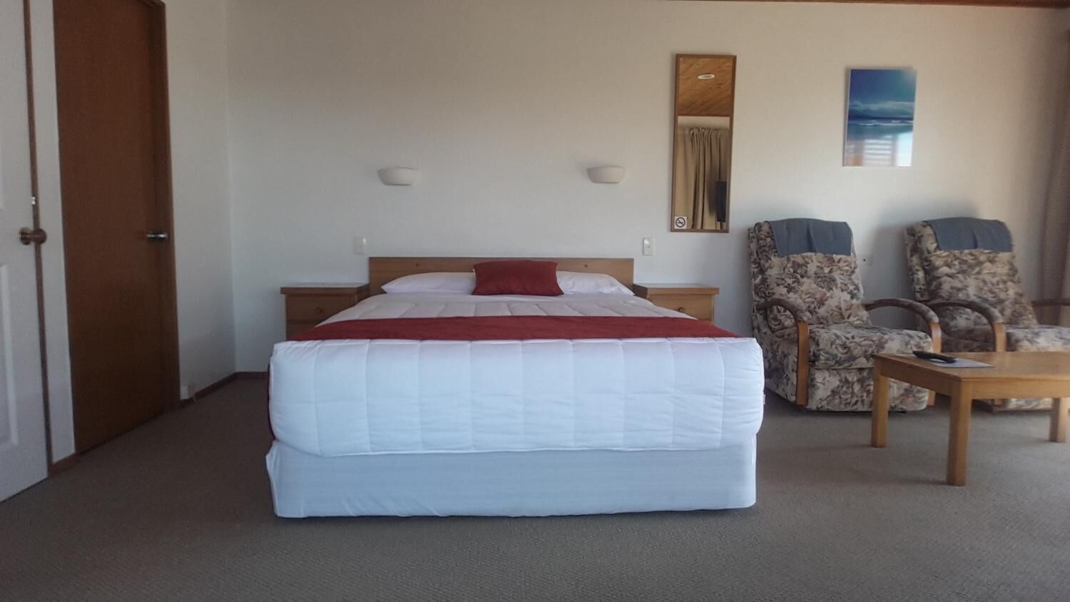 A hotel room with a large bed, two chairs, a small table, and a wall-mounted mirror.
