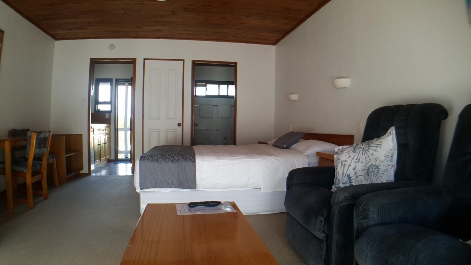 A room with a bed, a sofa, a wooden table, and a desk with chairs. There are two doors and a window.