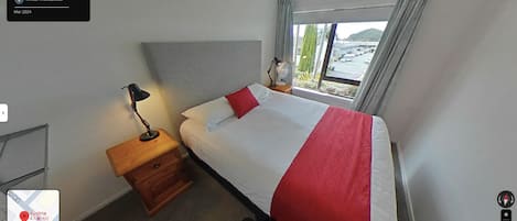 Une chambre d’hôtel trois étoiles comprenant un lit, une table de chevet, une lampe et une fenêtre donnant sur un paysage agréable.