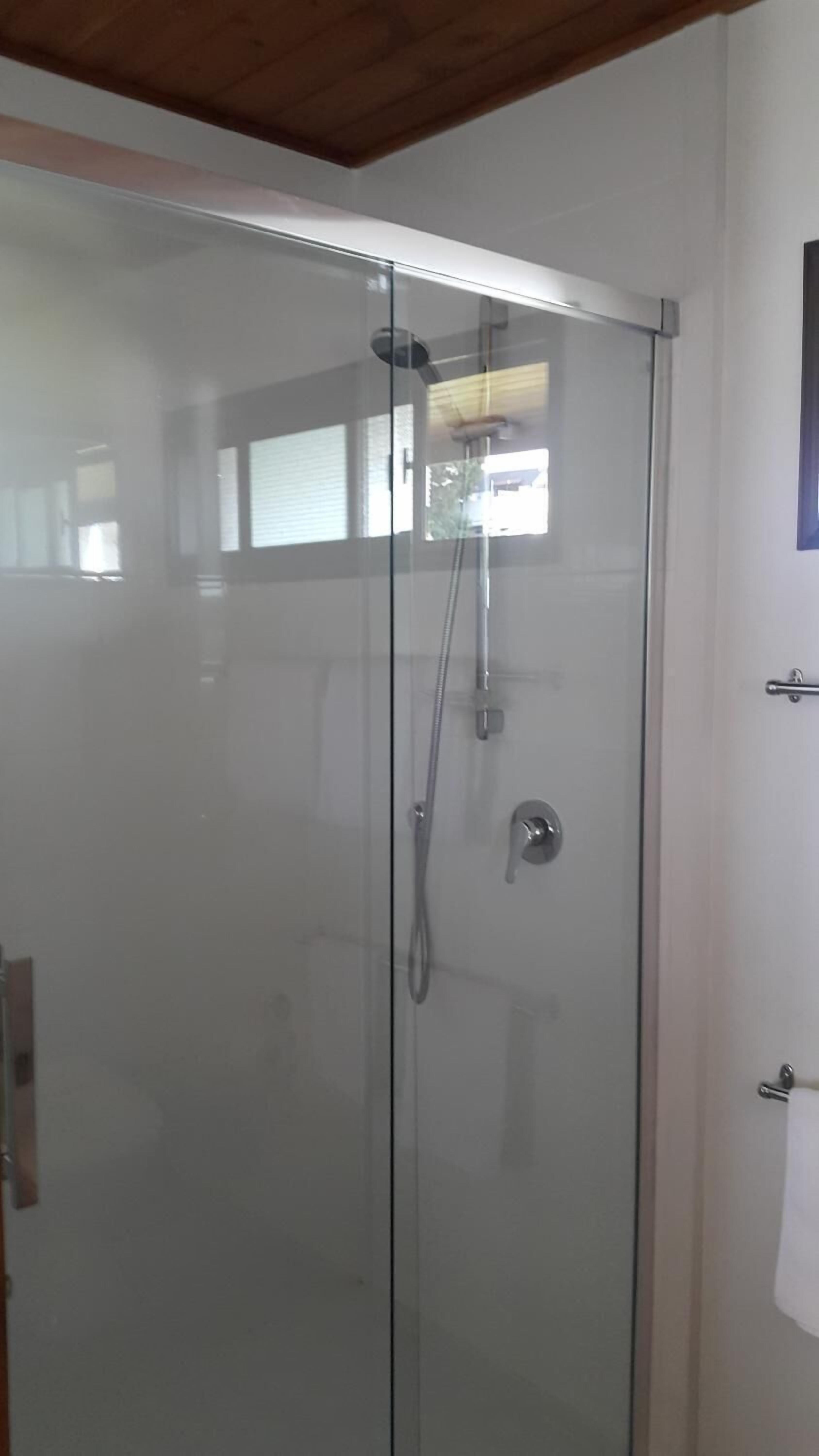 Une douche fermée par des parois en verre, équipée d’un pommeau de douche à main et d’un pommeau de douche fixe.