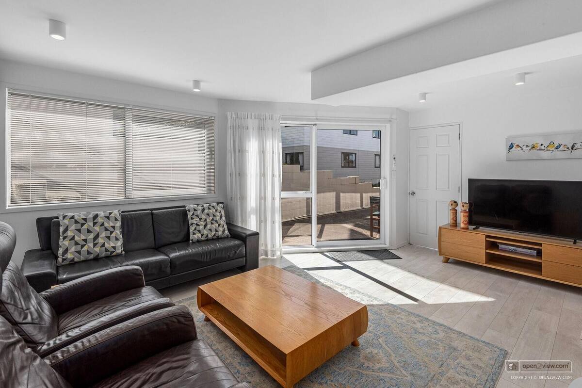 A modern living room with a leather sofa, a wooden coffee table, a flat-screen TV, and a sliding glass door leading to a balcony.